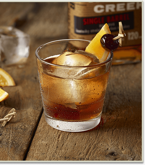 Dark liquor drink with an orange and a cherry in it