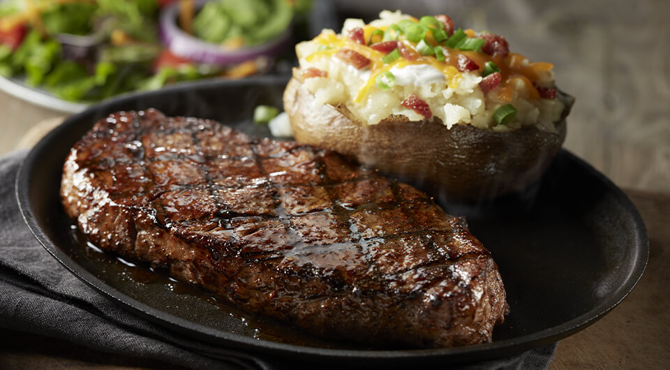 The New York Strip steak on a plate with a loaded potato.