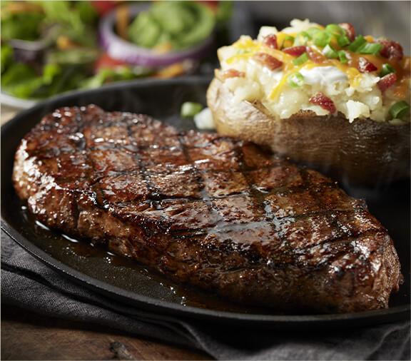 The New York Strip steak on a plate with a loaded potato.