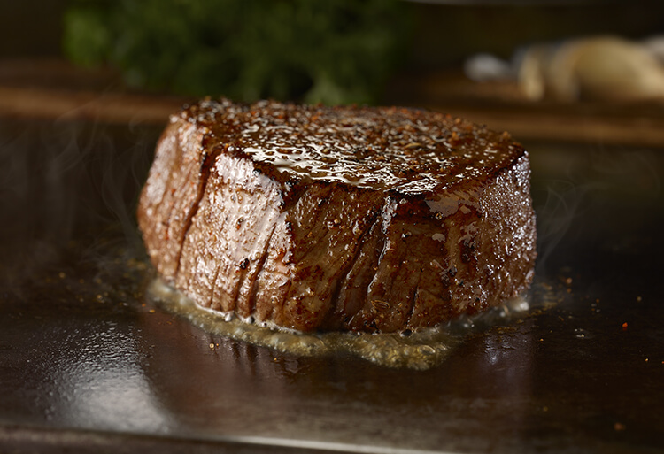 Picture of a steak being cooked on a skillet with ingredients in the background
