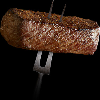 A two pronged fork with a cooked steak impaled on it