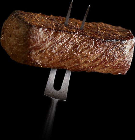 A two pronged fork with a cooked steak impaled on it